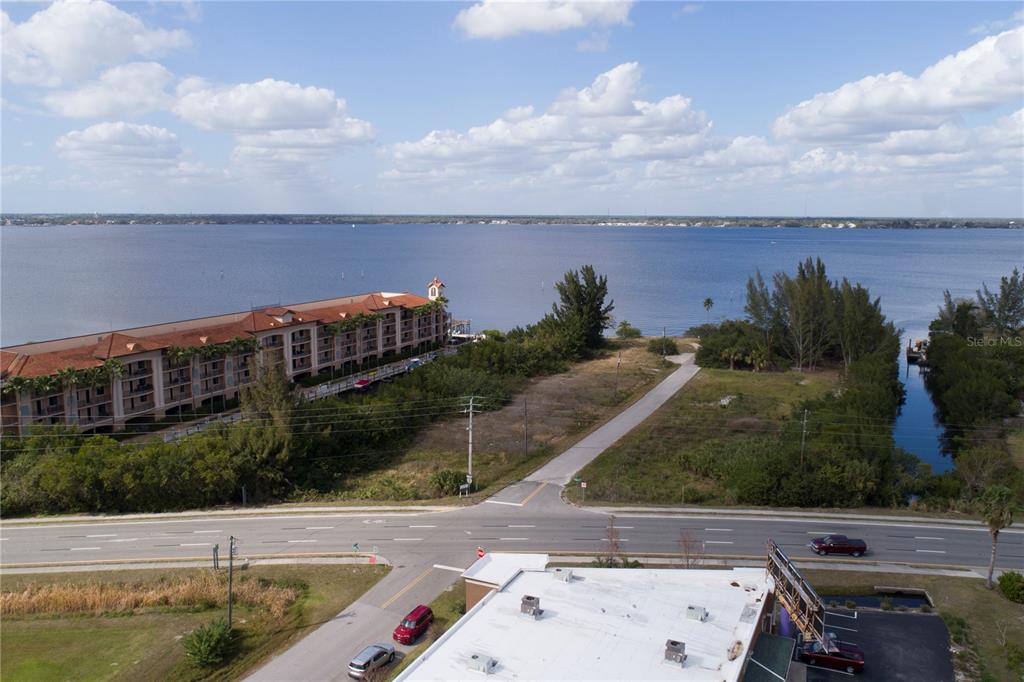 An aerial view shows a multi-story building, a vacant lot, and a road near water — 6162 LANDINGS WAY, PUNTA GORDA, FL