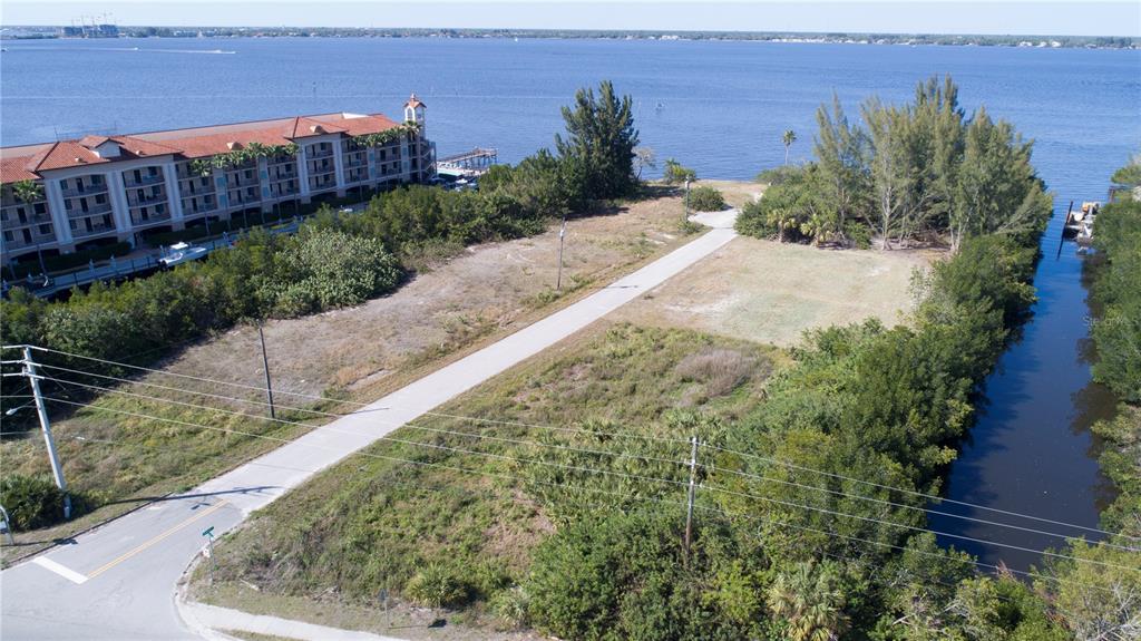 An aerial view shows a vacant, grassy lot bordered by a road, trees, and water — 6162 LANDINGS WAY, PUNTA GORDA, FL