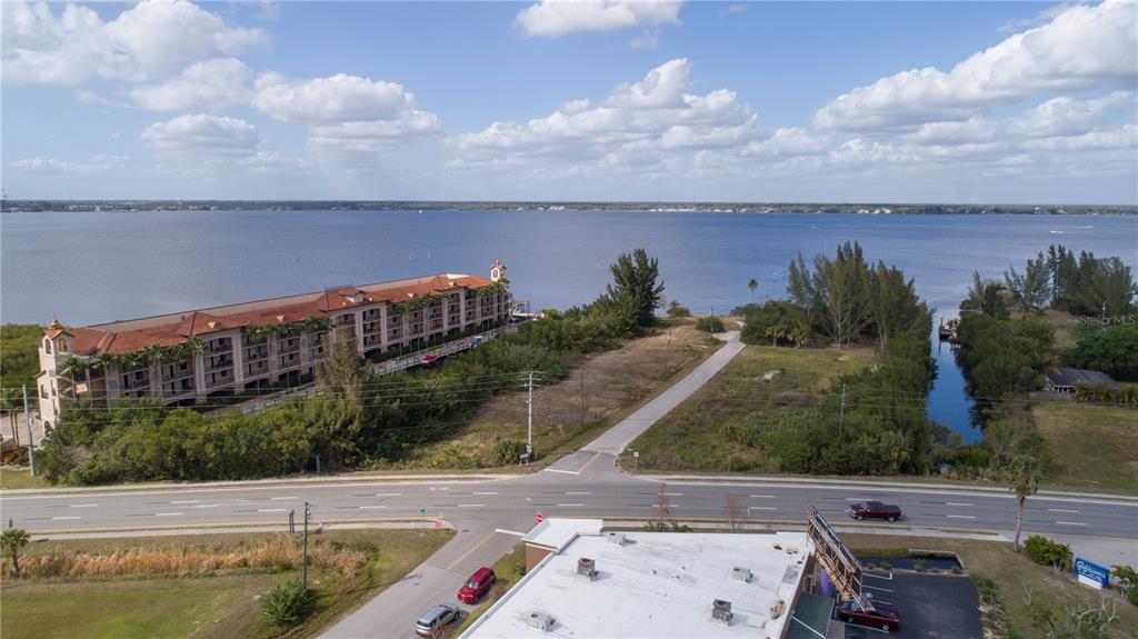 An aerial view shows a multi-story building, a vacant lot, and a road near water — 6162 LANDINGS WAY, PUNTA GORDA, FL