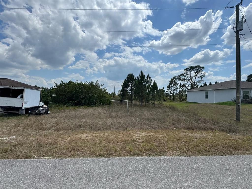 A vacant, grassy residential lot features a small soccer goal and neighboring houses — 942 ARDMORE STREET, LEHIGH ACRES, FL