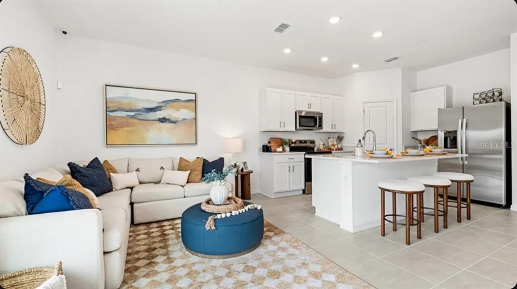An open-concept living room and kitchen featuring white cabinetry, stainless steel appliances, and blue accents — 10689 ECLIPSE STREET, SARASOTA, FL