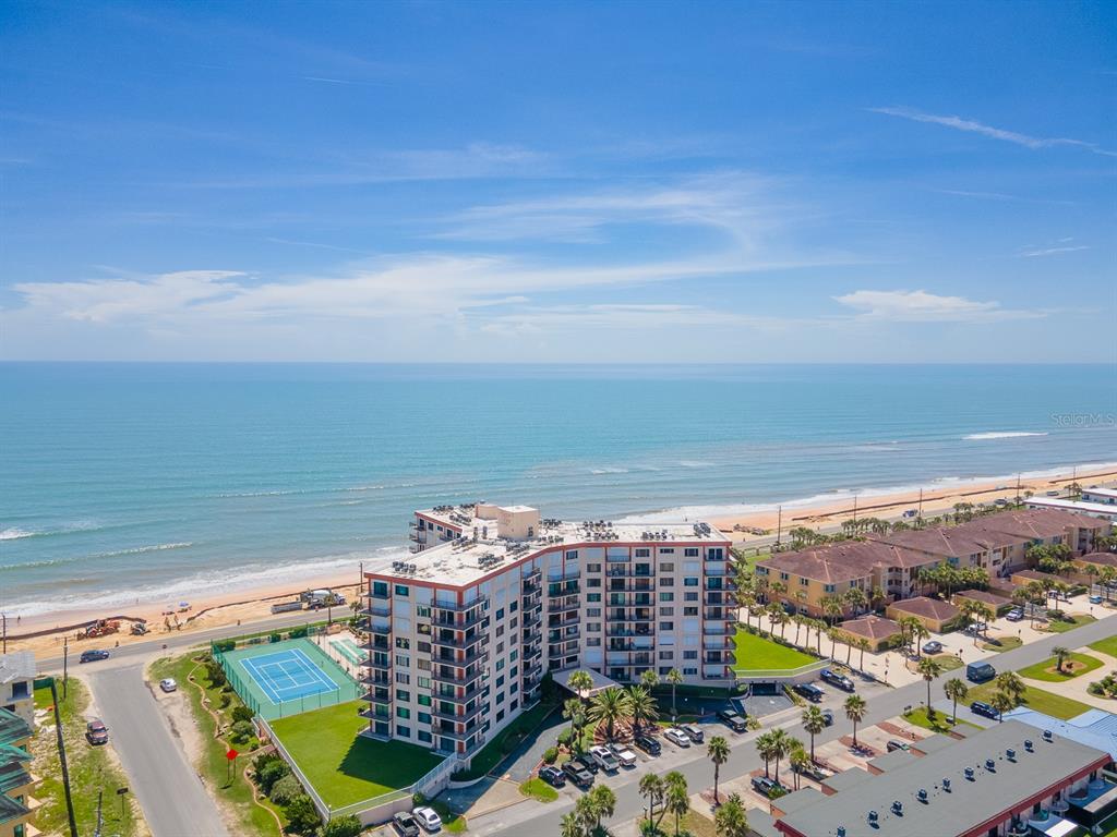 An aerial view shows a multi-story beachfront condominium building with a tennis court and ocean — 3600 S OCEAN SHORE BOULEVARD UNIT 720, FLAGLER BEACH, FL