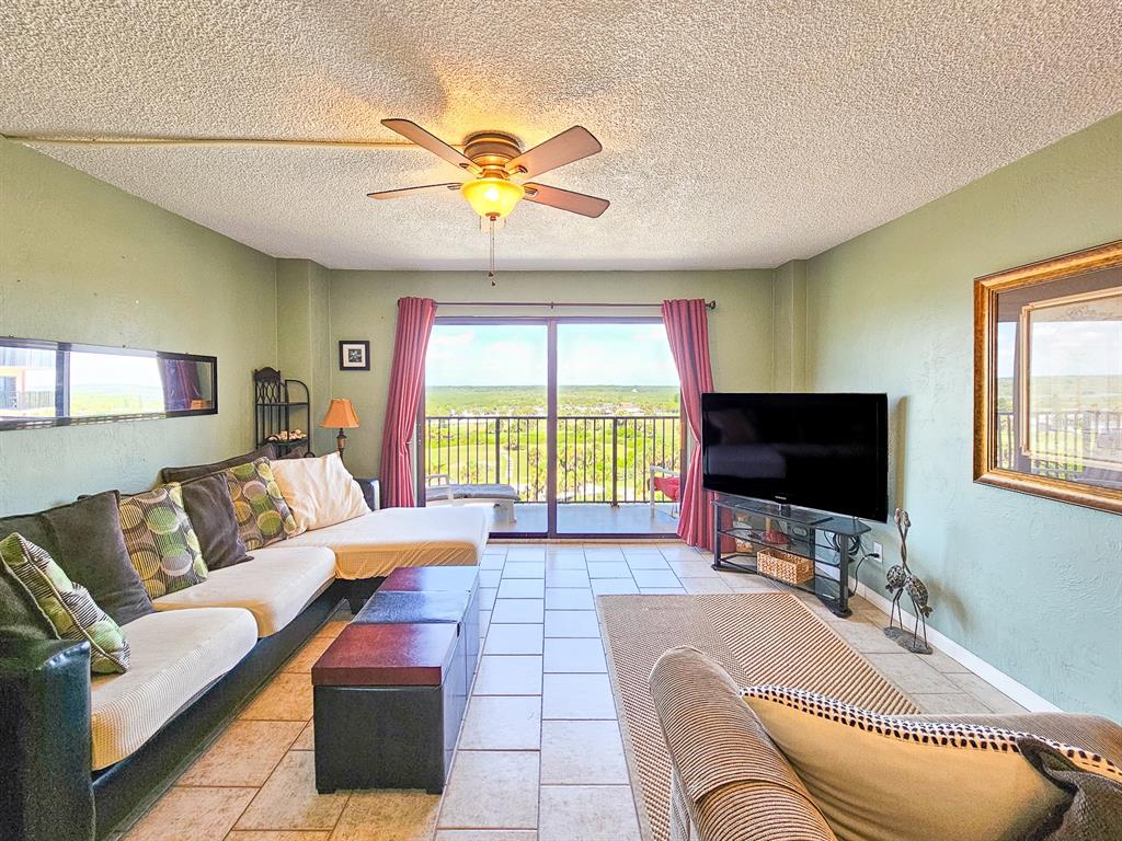 A living room features tile floors, a sectional sofa, a television, and a balcony view — 3600 S OCEAN SHORE BOULEVARD UNIT 720, FLAGLER BEACH, FL