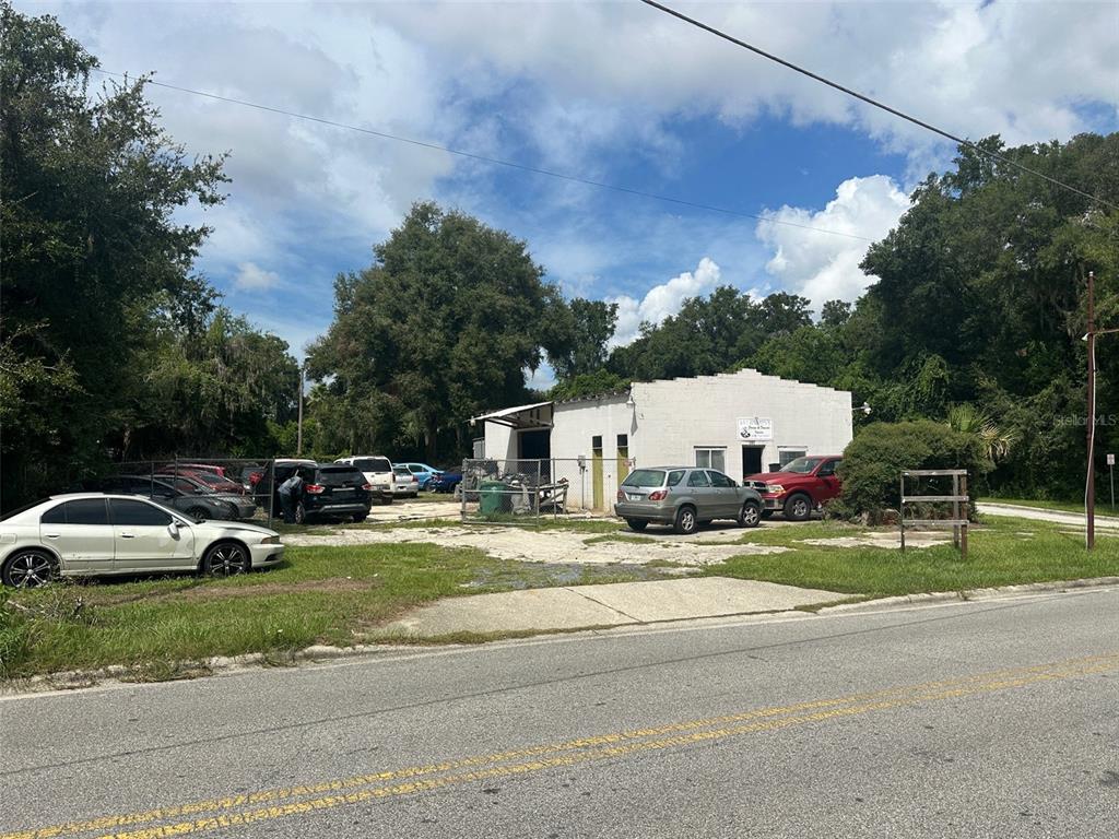 A white commercial building with a fenced lot containing several parked cars — 800 S ADELLE AVENUE, DELAND, FL