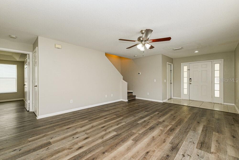 An empty living room features wood-look flooring, a ceiling fan, and a staircase — 1818 HORSECHESTNUT COURT, NEW PORT RICHEY, FL