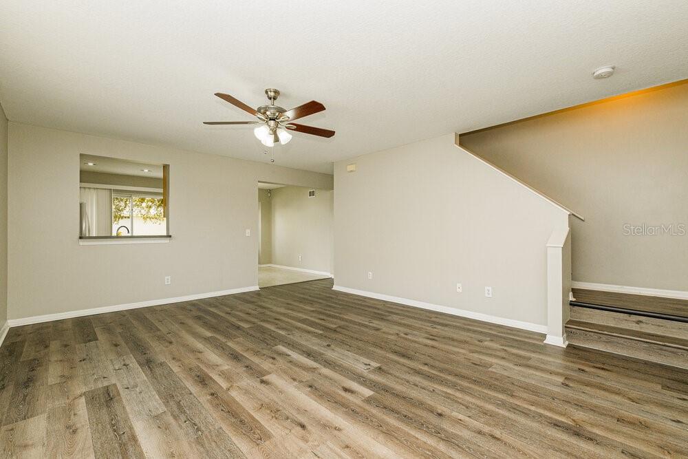 An empty living room features wood-look flooring, a ceiling fan, and stairs leading upward — 1818 HORSECHESTNUT COURT, NEW PORT RICHEY, FL