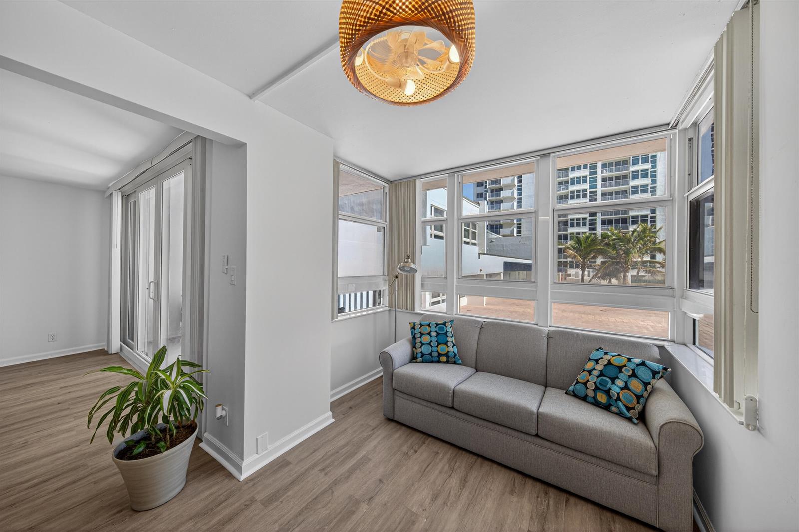 A living room features light wood flooring, a grey sofa, and large windows with exterior views — 1370 S Ocean Boulevard # 306, Pompano Beach FL 33062, POMPANO BEACH, FL