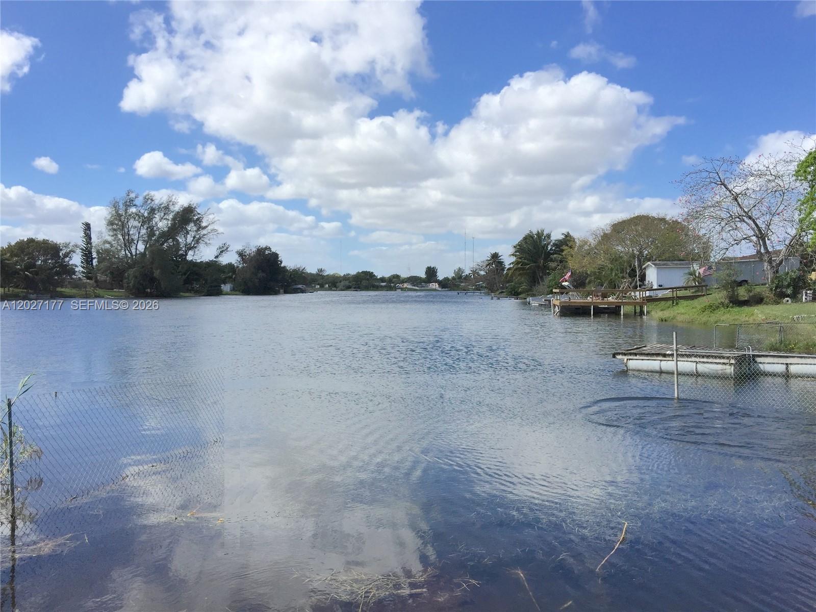 A view of a calm lake with a wooden dock and a chain-link fence — 3300 SW 32nd Ave, West Park FL 33023, WEST PARK, FL