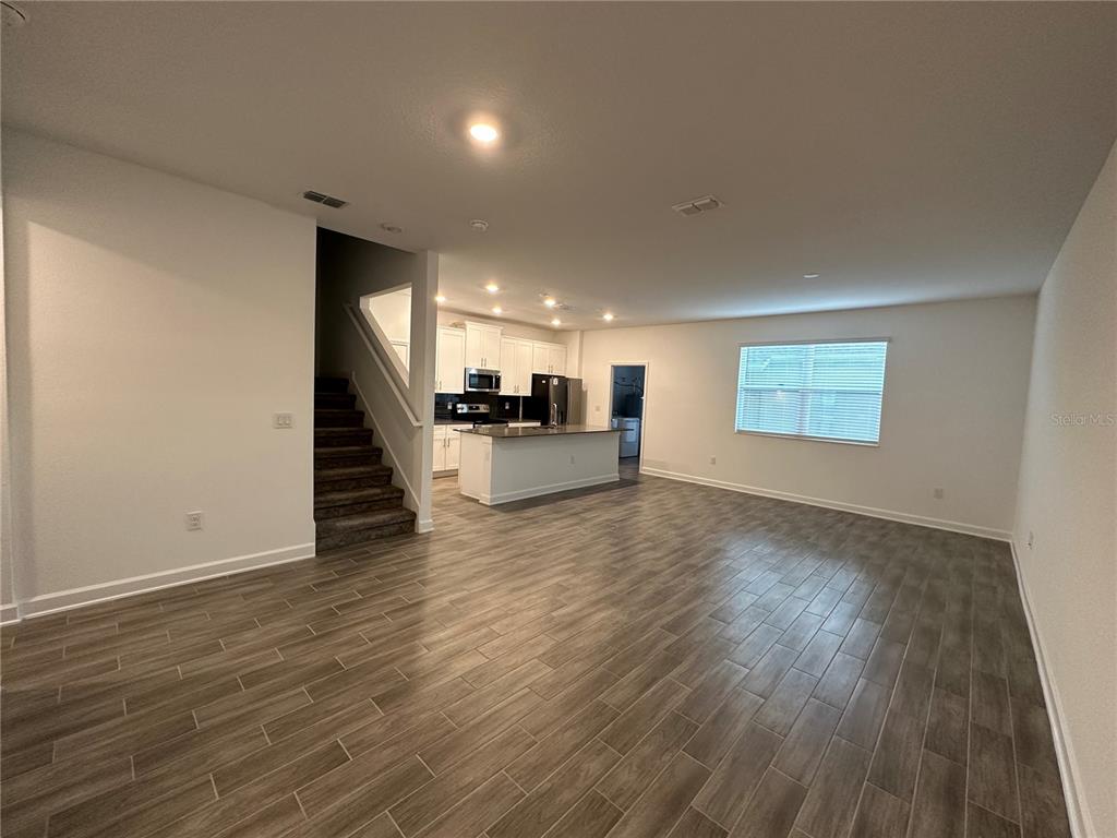An open-concept living area features wood-look tile flooring, a kitchen island, and a staircase — 3068 ADDISON BOULEVARD, ST CLOUD, FL