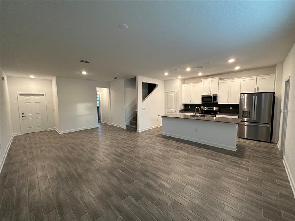 An open-concept kitchen and living area feature wood-look tile flooring and white cabinetry — 3068 ADDISON BOULEVARD, ST CLOUD, FL
