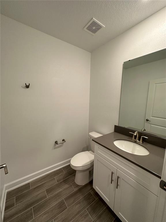 A bathroom features a white vanity with a dark countertop, a toilet, and wood-look flooring — 3068 ADDISON BOULEVARD, ST CLOUD, FL