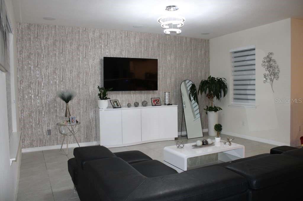 A living room features a textured accent wall, a wall-mounted television, and a white console — 1723 FLOURISH AVENUE, KISSIMMEE, FL