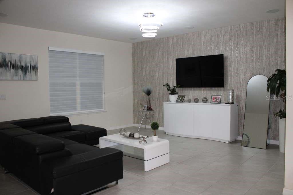A living room features a black sectional sofa, white coffee table, and a wall-mounted television — 1723 FLOURISH AVENUE, KISSIMMEE, FL