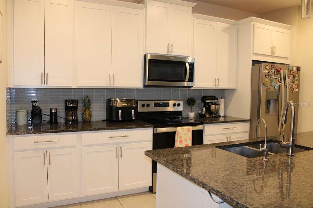 A kitchen with white cabinets, granite countertops, stainless steel appliances, and a gray tile backsplash — 1723 FLOURISH AVENUE, KISSIMMEE, FL