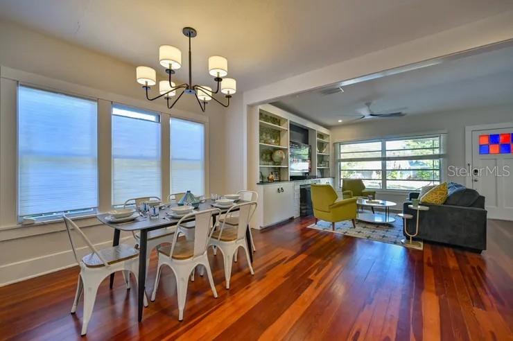 An open-concept dining and living area features hardwood floors, a chandelier, and built-in shelving — 2408 HILLVIEW STREET, SARASOTA, FL