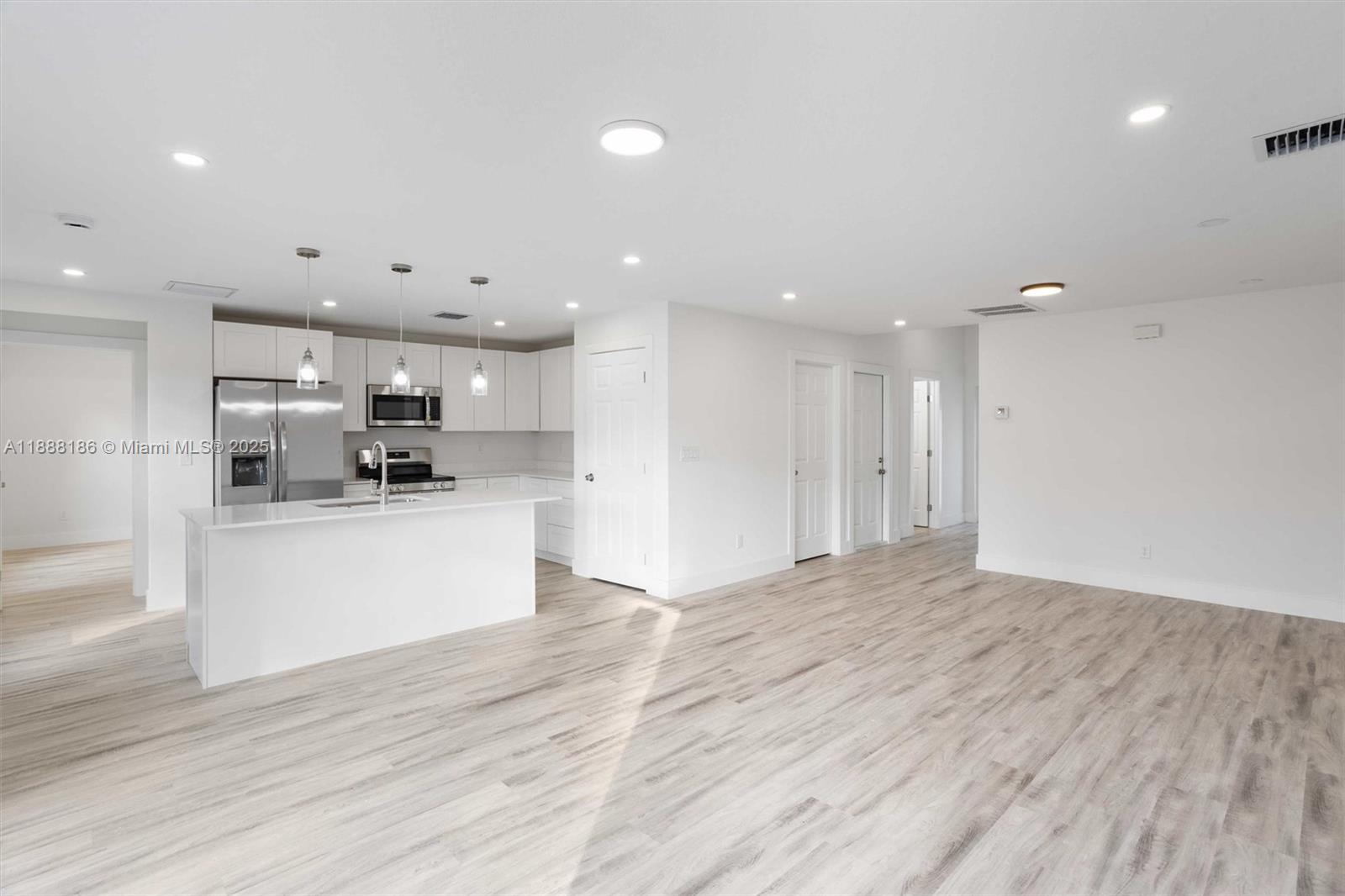 A modern kitchen with white cabinetry and an island opens to a spacious living area — 1150 SE Tarleton St, Palm Bay FL 32909, PALM BAY, FL
