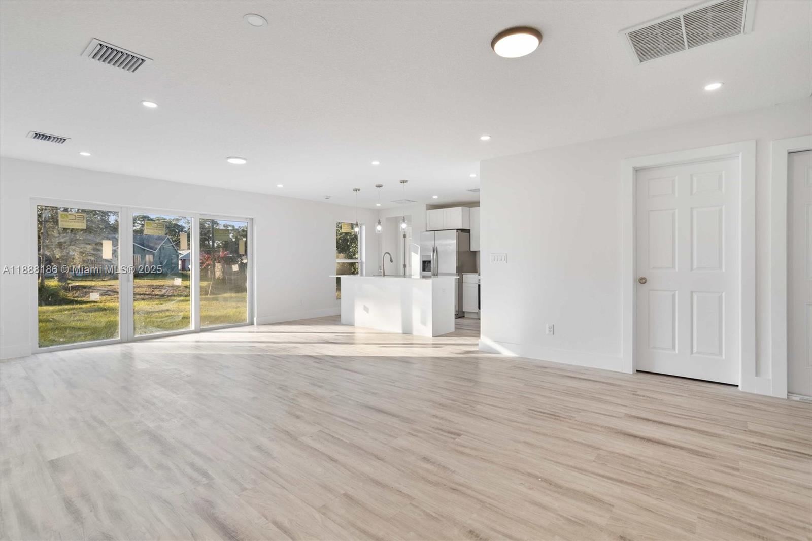 An open-concept living area features light wood-look flooring, white walls, and a modern kitchen island — 1150 SE Tarleton St, Palm Bay FL 32909, PALM BAY, FL