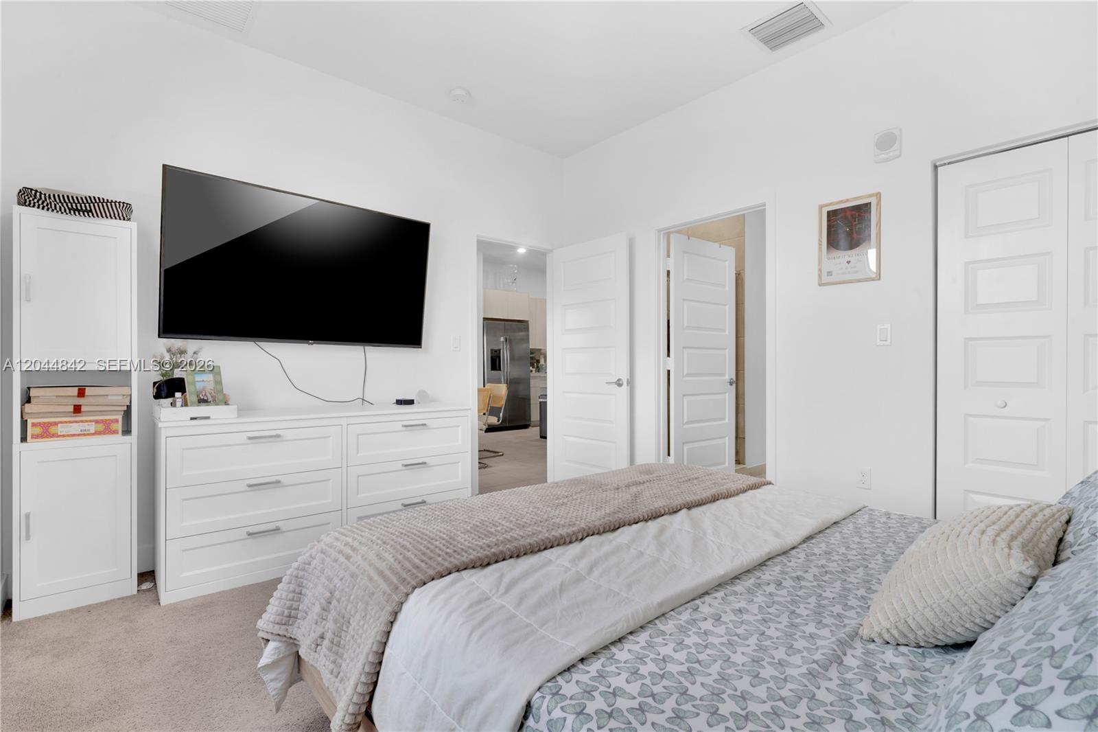 A bedroom features a white dresser, a wall-mounted television, and a bed with patterned bedding — 7819 NW 104th Ave # 23, Doral FL 33178, DORAL, FL