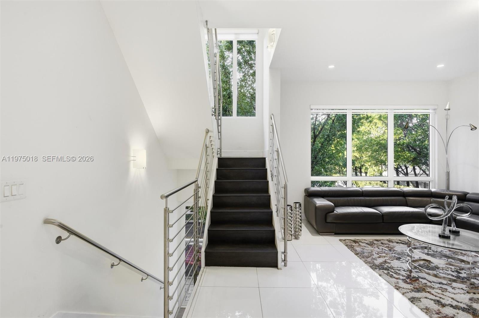 A modern living room features a dark staircase, white tile floors, and large windows — 6671 NW 105th Pl # 6671, Doral FL 33178, DORAL, FL