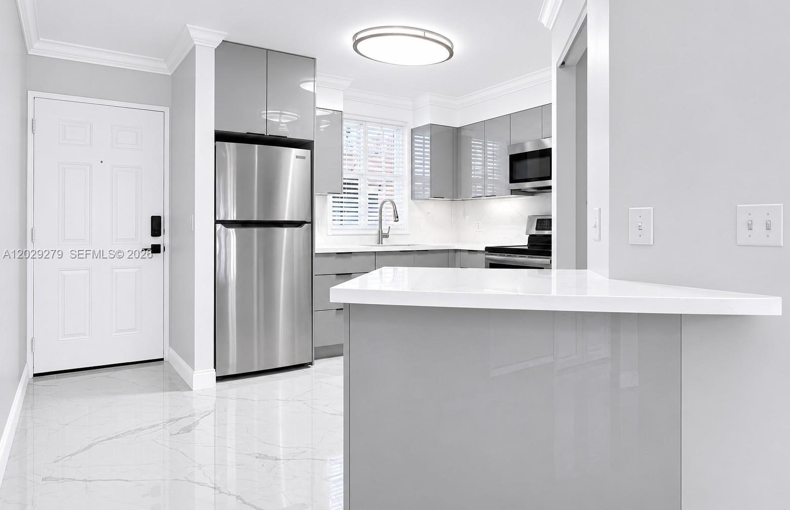 A modern kitchen features gray glossy cabinets, stainless steel appliances, and white marble-patterned tile floors — 6135 NW 186th St # 202, Hialeah FL 33015, HIALEAH, FL