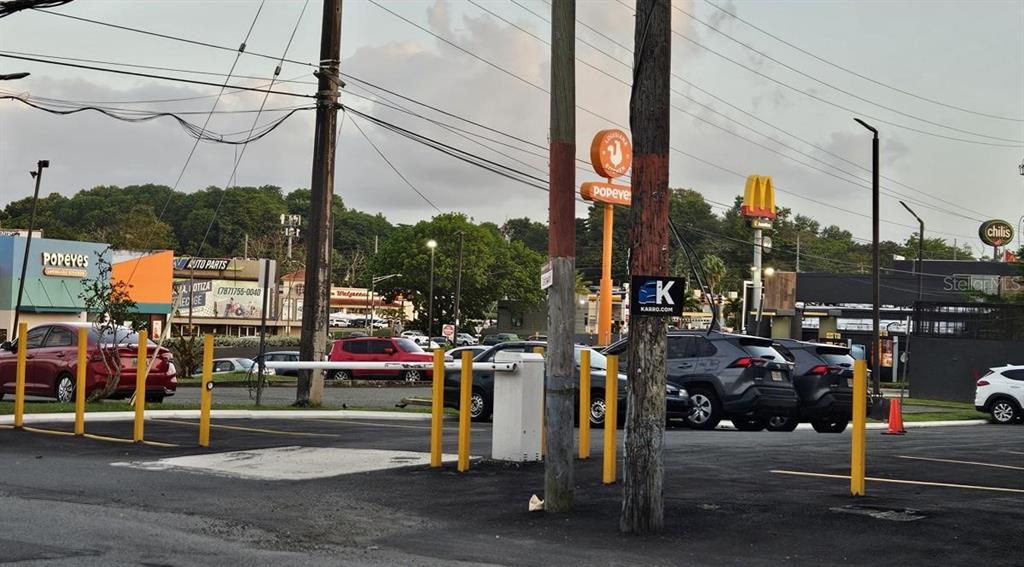 An outdoor parking lot with yellow bollards, a security gate, and various nearby restaurant signs — 863 CARR. 876, TRUJILLO ALTO, PR