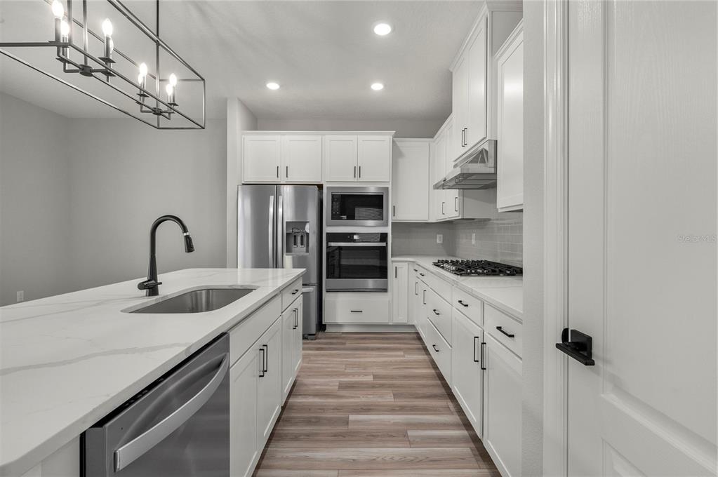 A modern kitchen features white cabinetry, stainless steel appliances, and a large marble-topped island — 7899 SOMERSWORTH DRIVE, KISSIMMEE, FL