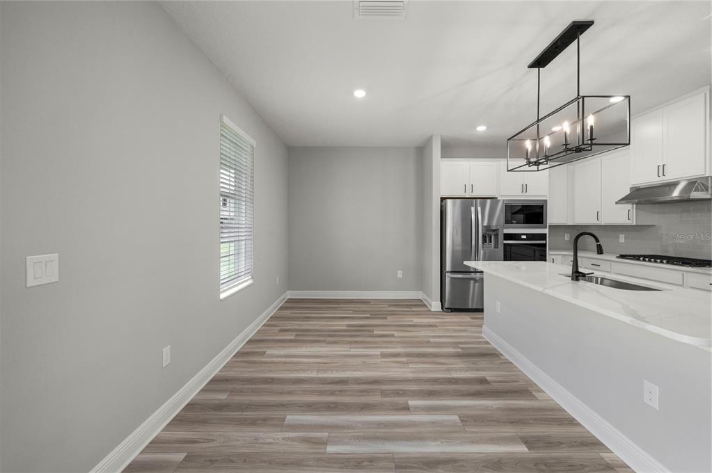 A kitchen with white cabinets, stainless steel appliances, and a dining area with wood flooring — 7899 SOMERSWORTH DRIVE, KISSIMMEE, FL