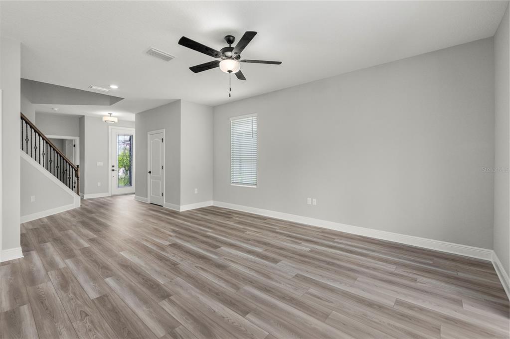 An empty living room features light gray walls, wood-look flooring, a ceiling fan, and stairs — 7899 SOMERSWORTH DRIVE, KISSIMMEE, FL