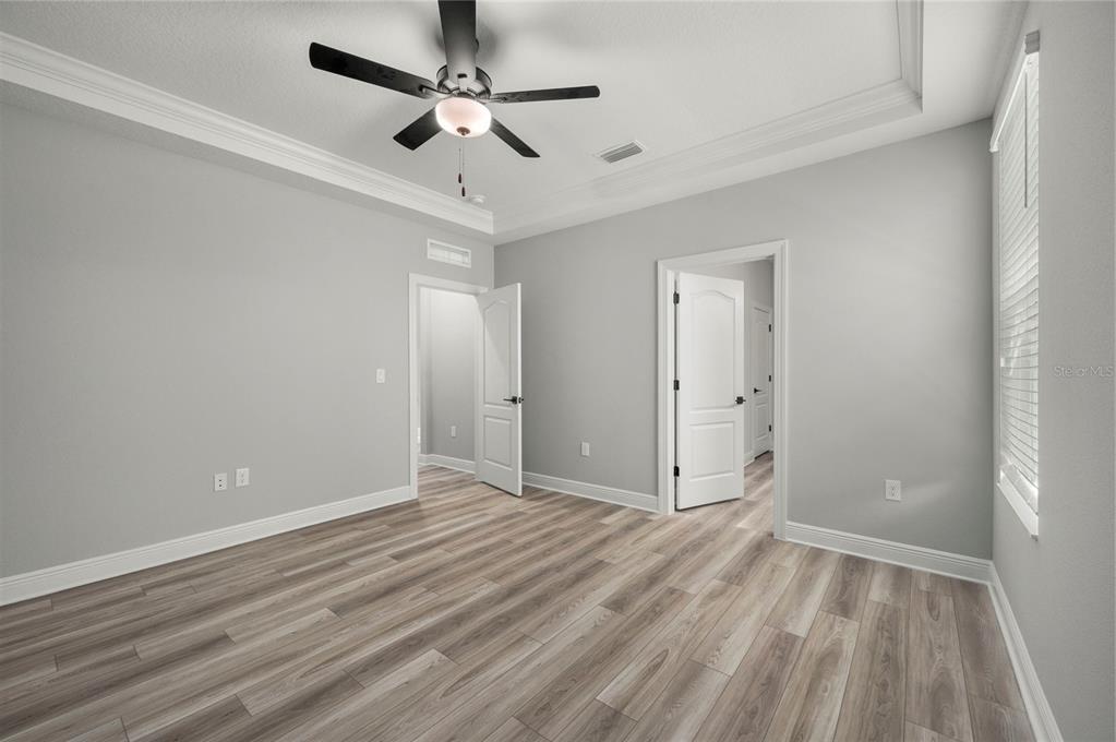 An empty bedroom features light gray walls, wood-look flooring, a ceiling fan, and two doorways — 7899 SOMERSWORTH DRIVE, KISSIMMEE, FL