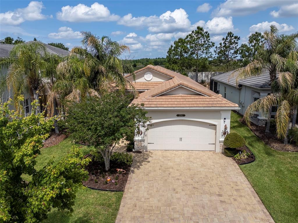 An aerial view of a single-story house with a tan tile roof and paver driveway — 2761 TARRAGONA WAY, WESLEY CHAPEL, FL