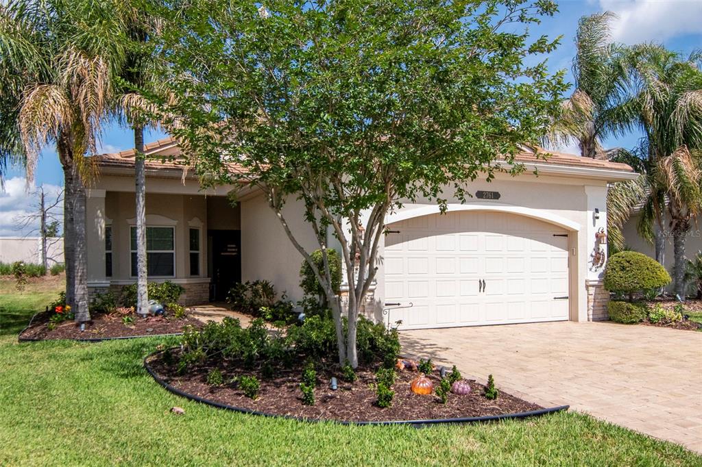 A single-story house with a beige stucco exterior, a two-car garage, and a landscaped front yard — 2761 TARRAGONA WAY, WESLEY CHAPEL, FL