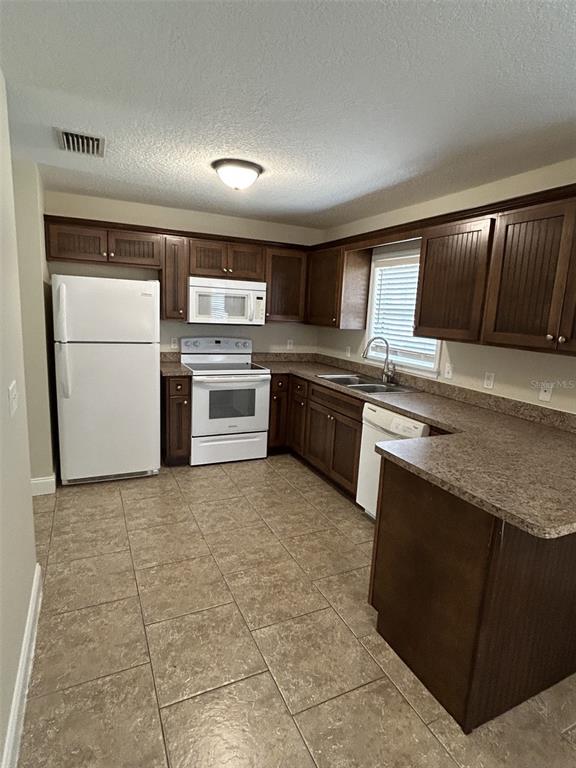 A kitchen features dark wood cabinets, white appliances, a double sink, and tan tile flooring — 119 W 10TH AVENUE, MOUNT DORA, FL