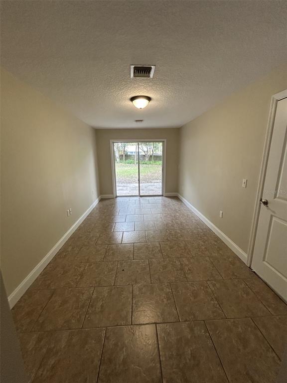 An empty room with tan tile flooring, beige walls, and sliding glass doors leading outside — 119 W 10TH AVENUE, MOUNT DORA, FL