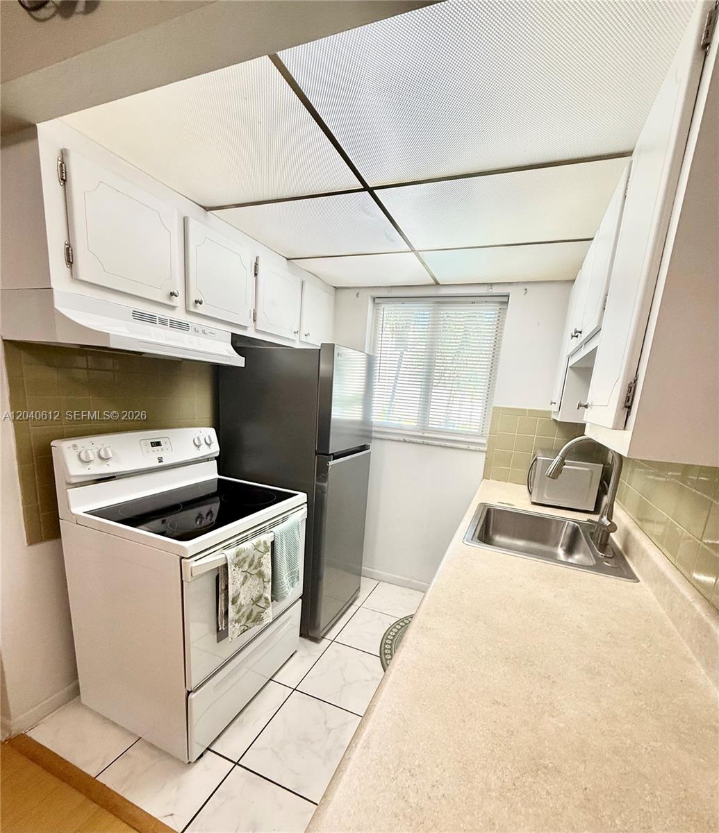A galley kitchen features white cabinets, a stainless steel refrigerator, and a white electric range — 2145 Pierce St # 206, Hollywood FL 33020, HOLLYWOOD, FL