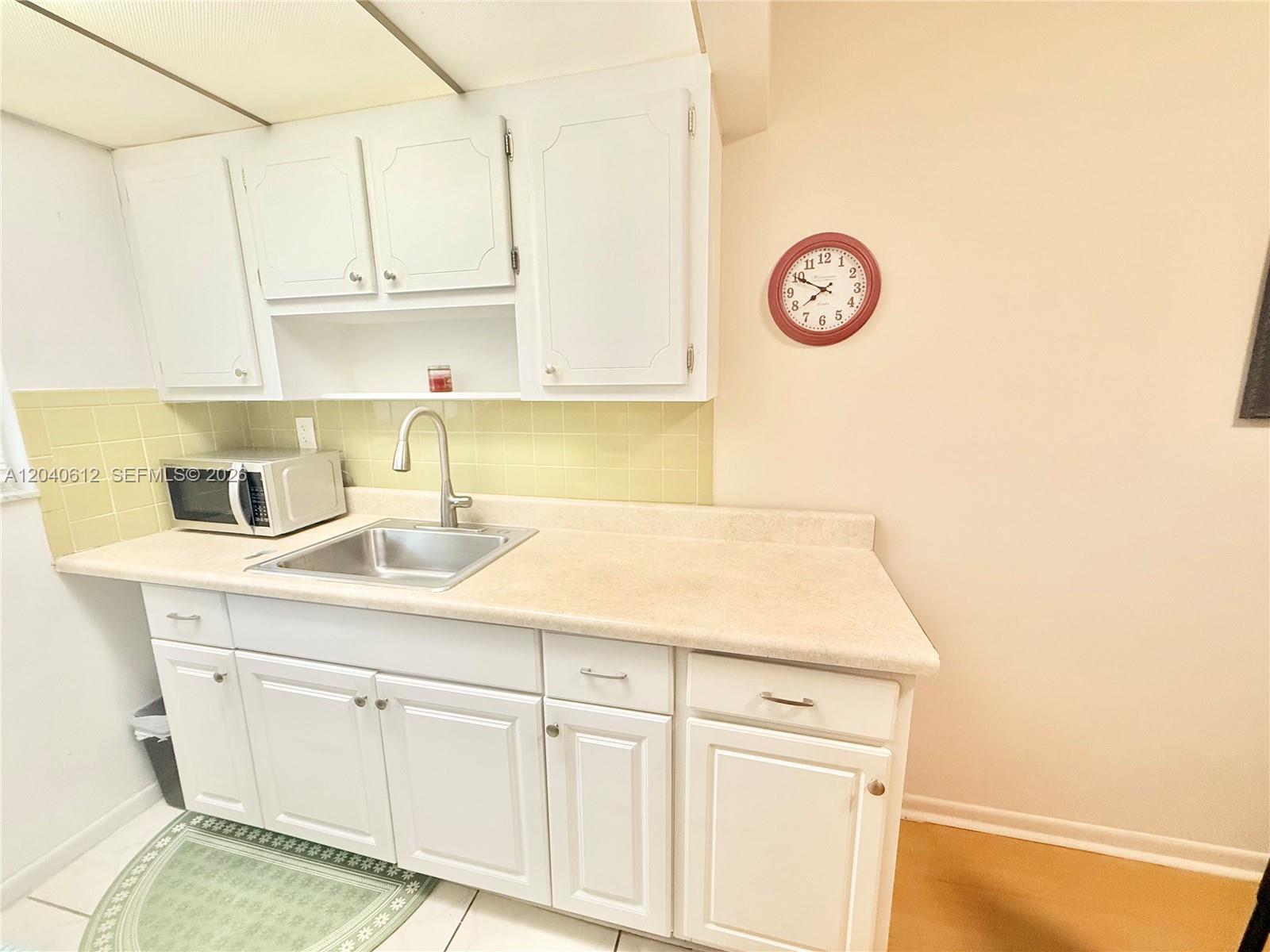A kitchen features white cabinets, a stainless steel sink, a microwave, and a wall clock — 2145 Pierce St # 206, Hollywood FL 33020, HOLLYWOOD, FL