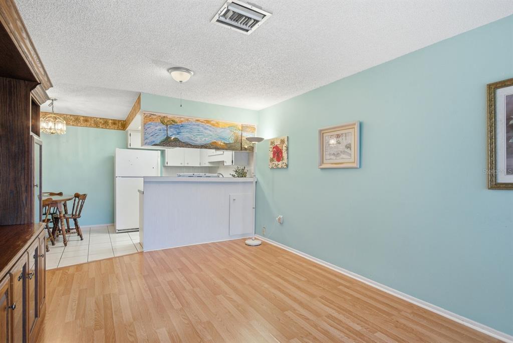 A dining and living area features light blue walls, wood-look flooring, and a kitchen pass-through — 4344 TAHITIAN GARDENS CIRCLE UNIT B, HOLIDAY, FL