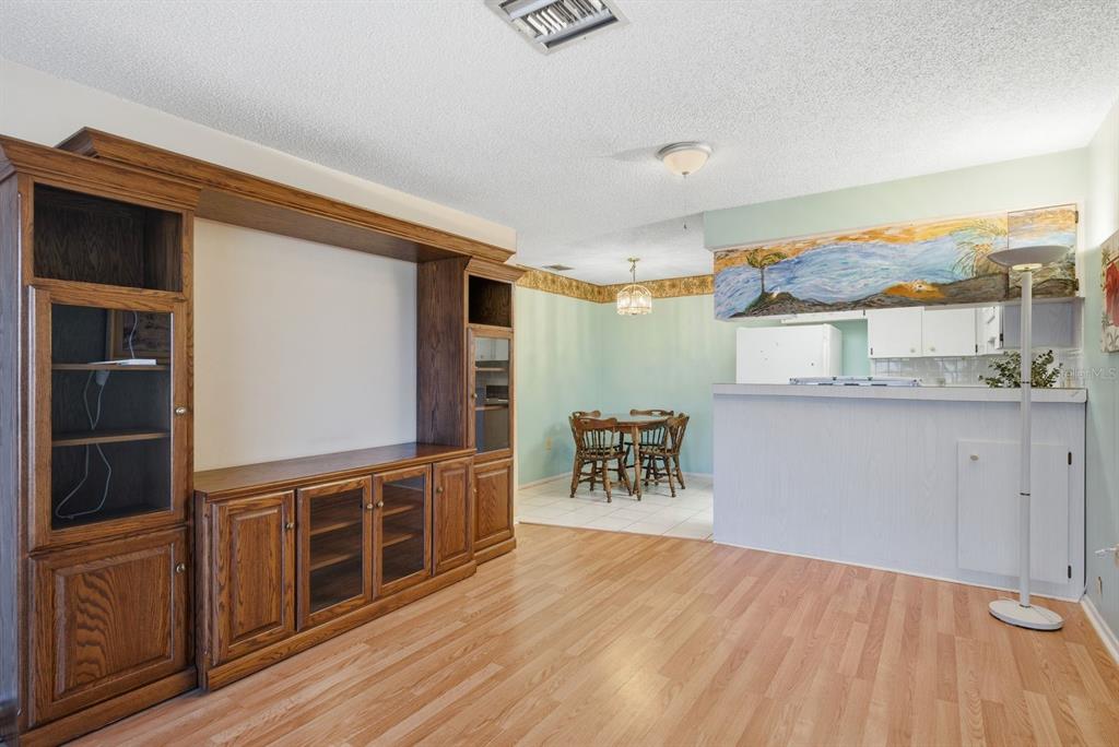 A living room with wood flooring and a large entertainment center opens to a dining area — 4344 TAHITIAN GARDENS CIRCLE UNIT B, HOLIDAY, FL