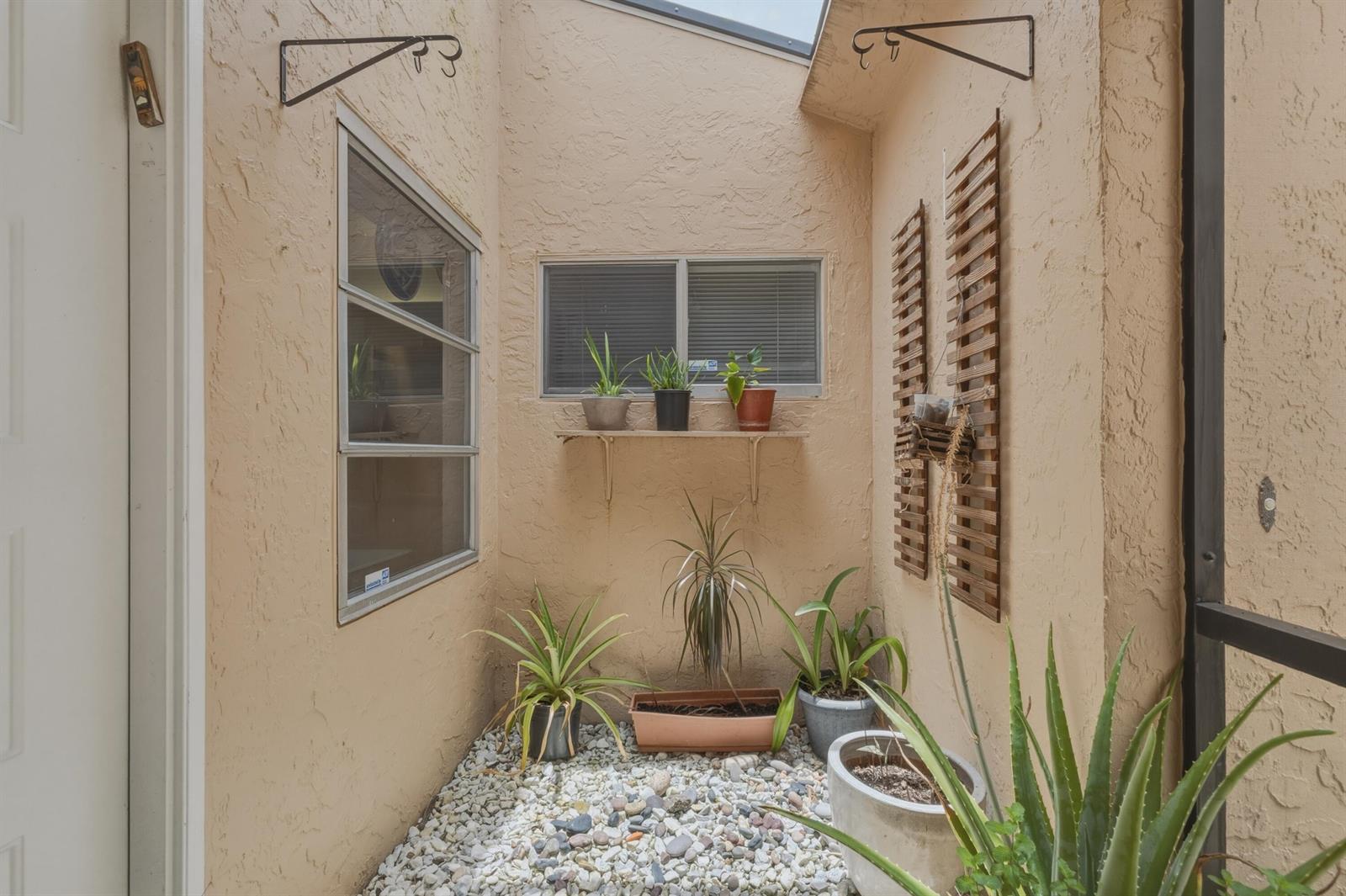 A small, enclosed outdoor courtyard features a gravel floor, potted plants, and wall-mounted shelves — 8128 Summerbreeze Lane, Boca Raton FL 33496, BOCA RATON, FL