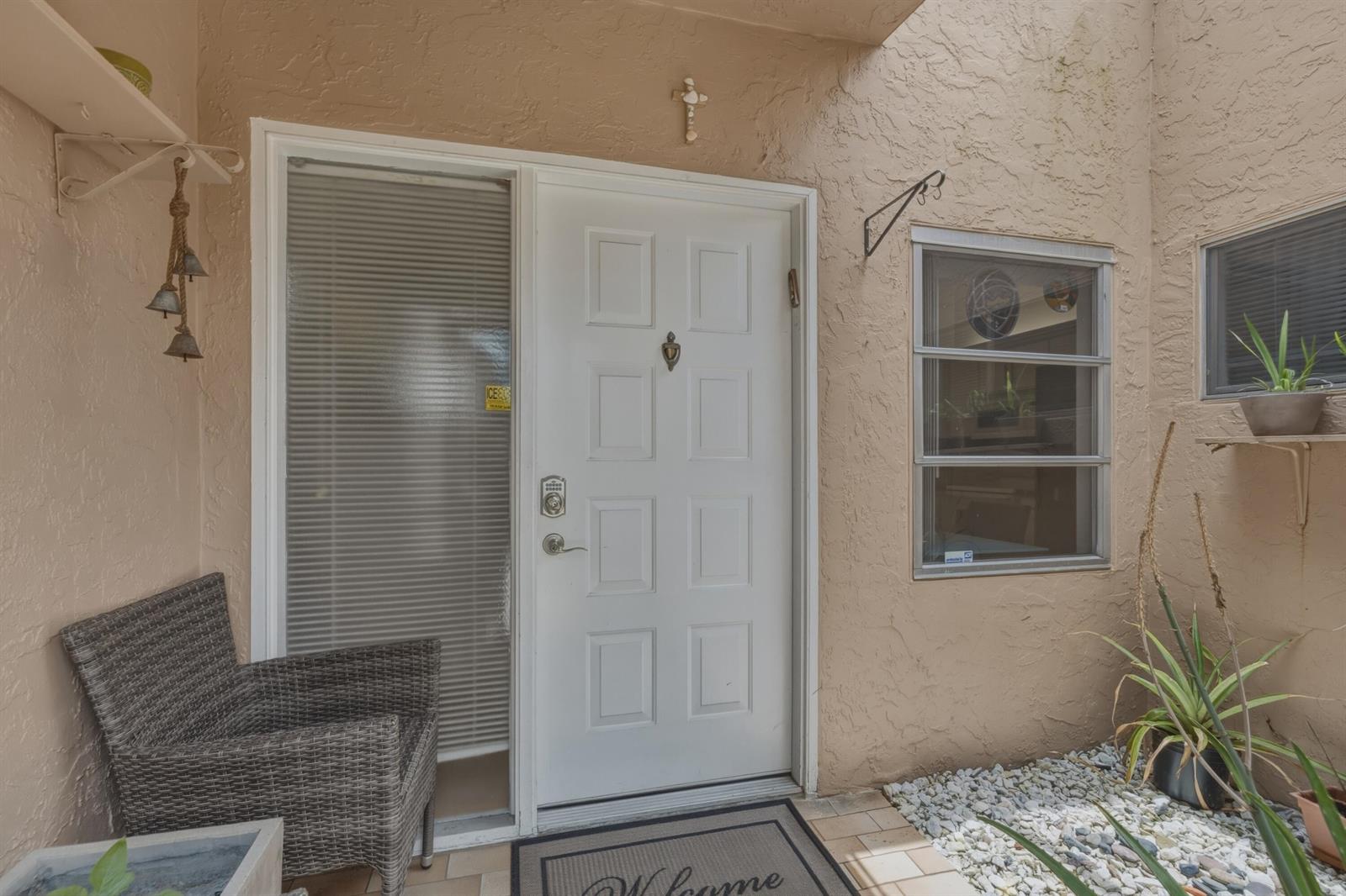 A white front door with a side window, a wicker chair, and gravel landscaping — 8128 Summerbreeze Lane, Boca Raton FL 33496, BOCA RATON, FL