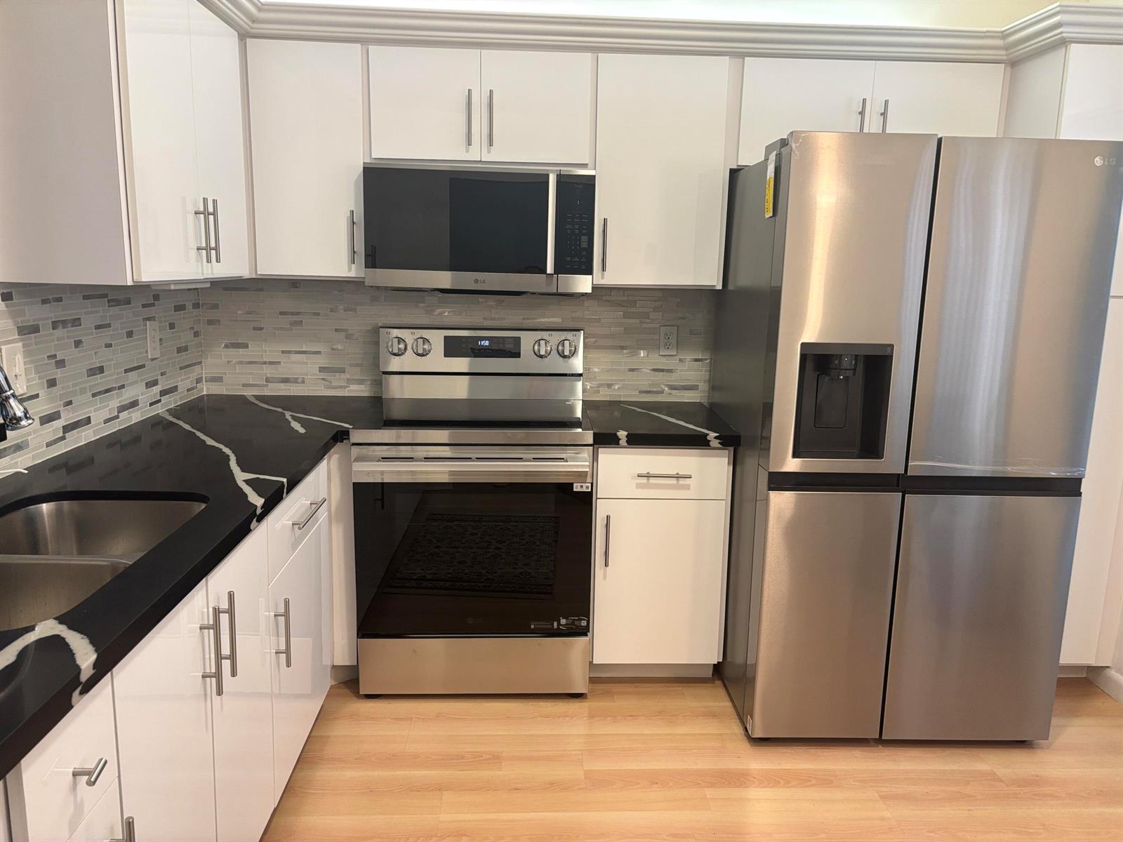 A kitchen features white cabinets, black countertops, stainless steel appliances, and a tiled backsplash — 8128 Summerbreeze Lane, Boca Raton FL 33496, BOCA RATON, FL