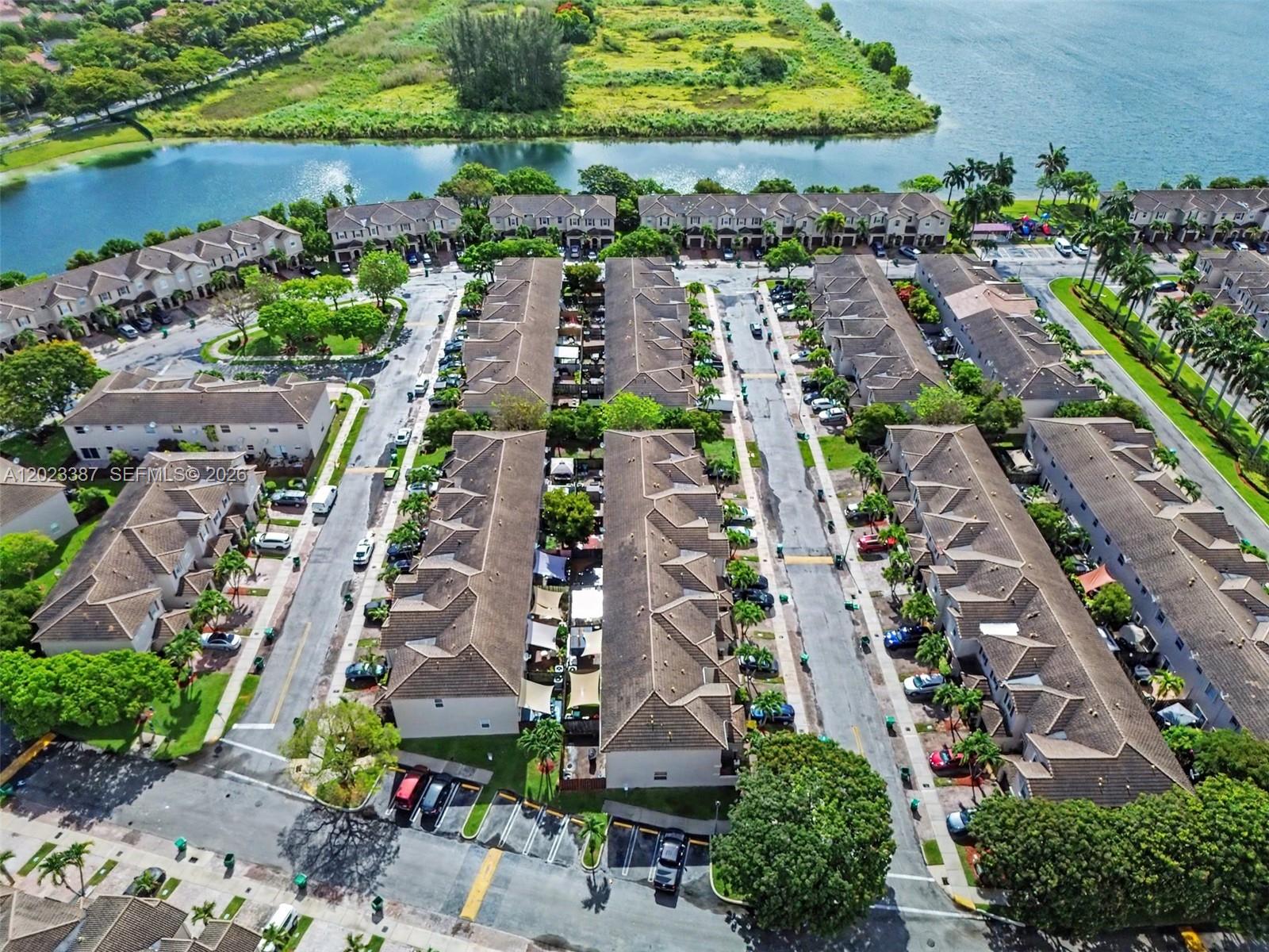 An aerial view shows multiple rows of townhouses with brown roofs near a lake — 9267 SW 220th Ter, Cutler Bay FL 33190, CUTLER BAY, FL