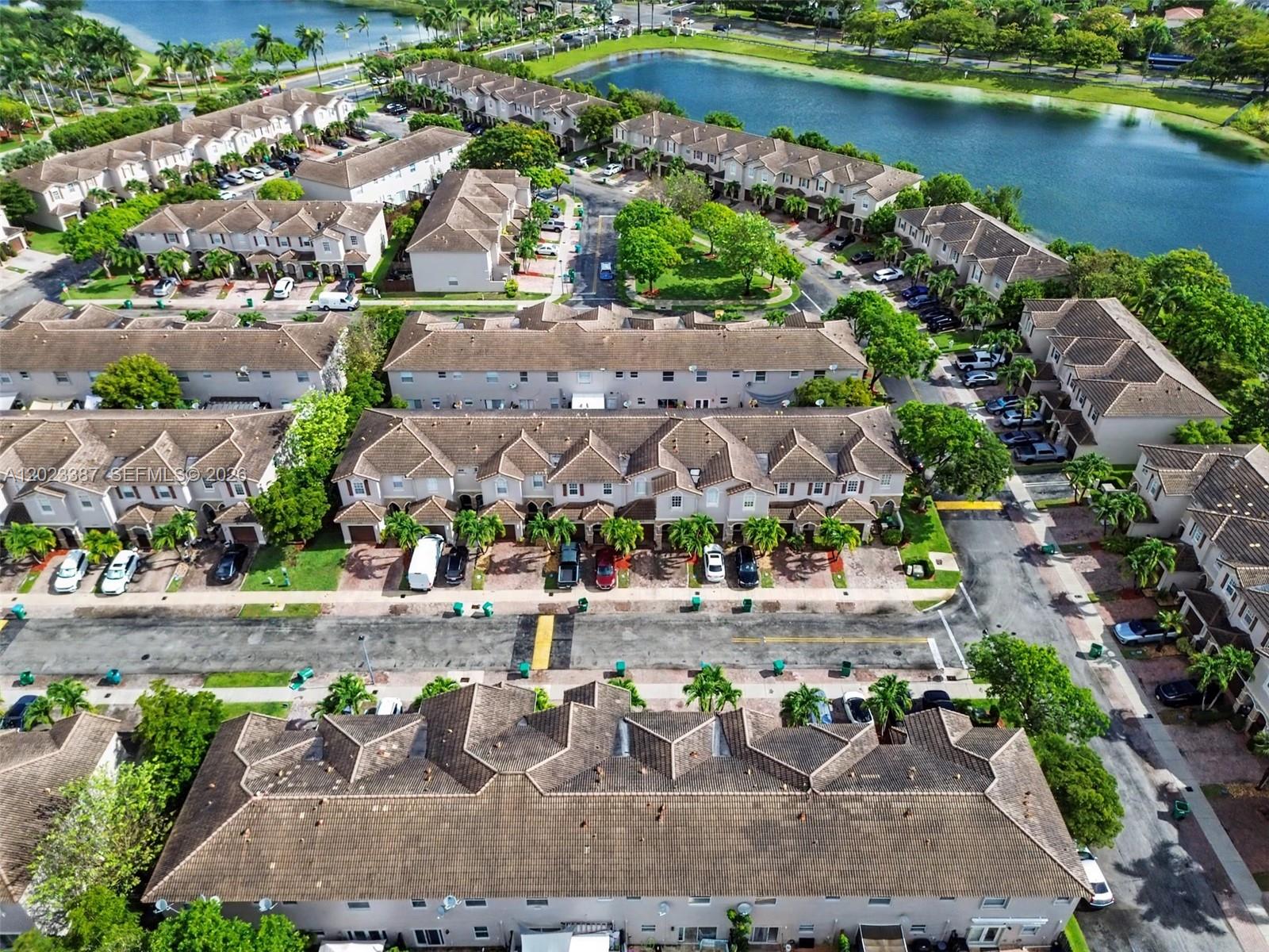 An aerial view shows multiple rows of townhouses with tiled roofs surrounding a central lake — 9267 SW 220th Ter, Cutler Bay FL 33190, CUTLER BAY, FL