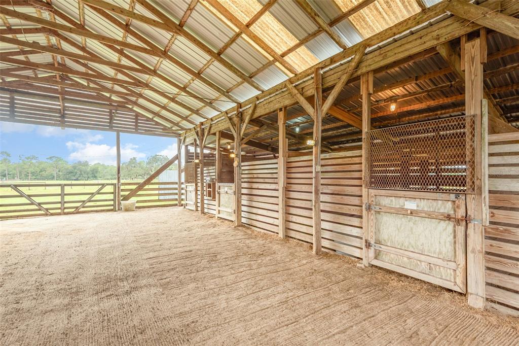 An open-air wooden horse barn features multiple stalls with metal mesh doors and dirt flooring — 1374 E OHIO AVENUE, LAKE HELEN, FL