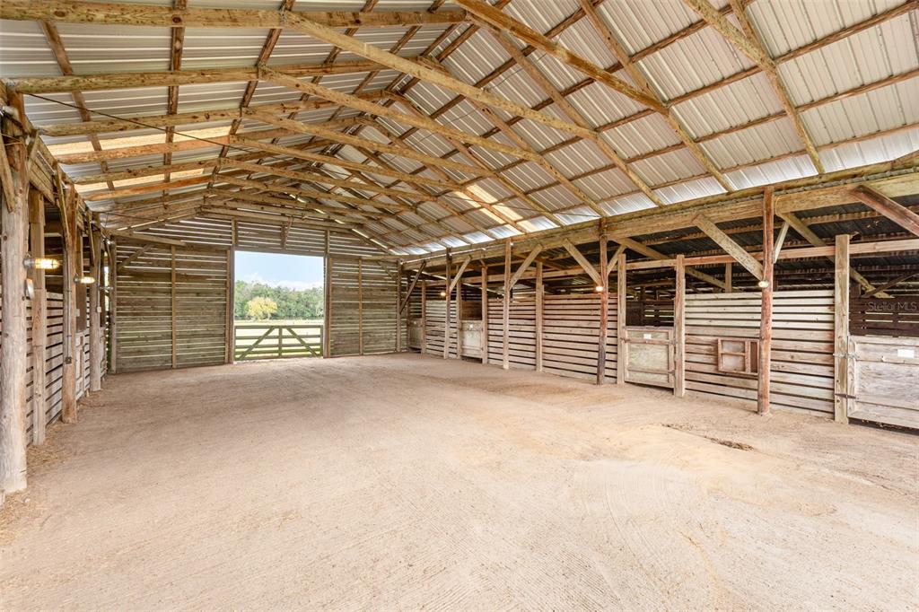 An interior view of a wooden barn featuring multiple horse stalls and a dirt floor — 1374 E OHIO AVENUE, LAKE HELEN, FL