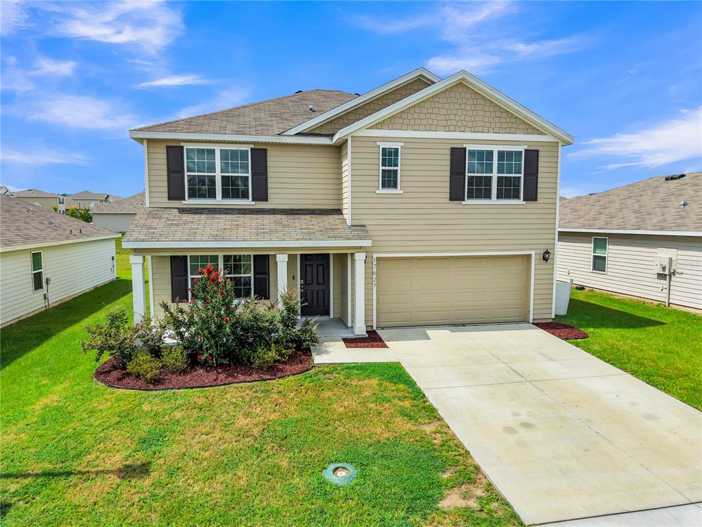 A two-story tan house with a front porch, a two-car garage, and a landscaped yard — 17627 NW 172ND AVENUE, ALACHUA, FL