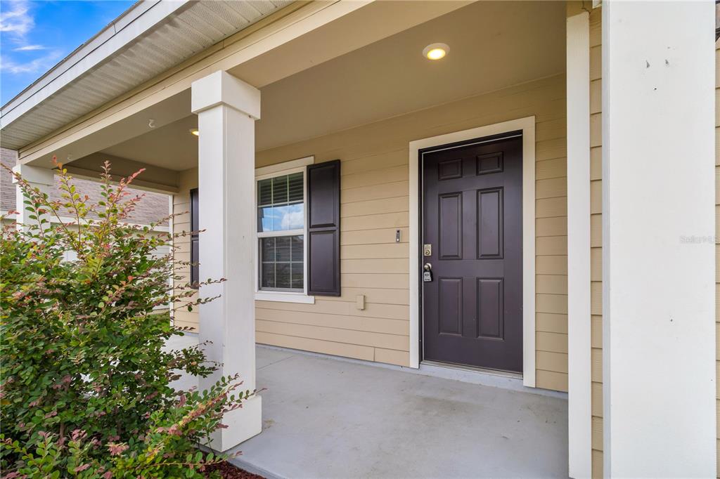 A covered front porch features a dark brown door, a window with shutters, and columns — 17627 NW 172ND AVENUE, ALACHUA, FL