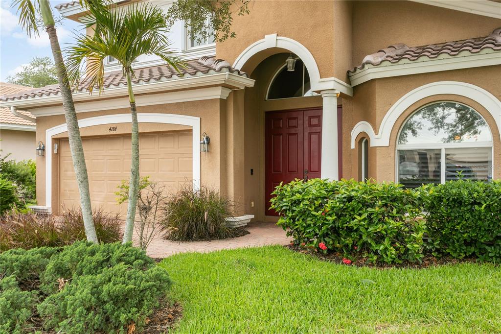 A tan two-story house features a red front door, a garage, and a landscaped yard — 4284 RIVER BANK WAY, PUNTA GORDA, FL