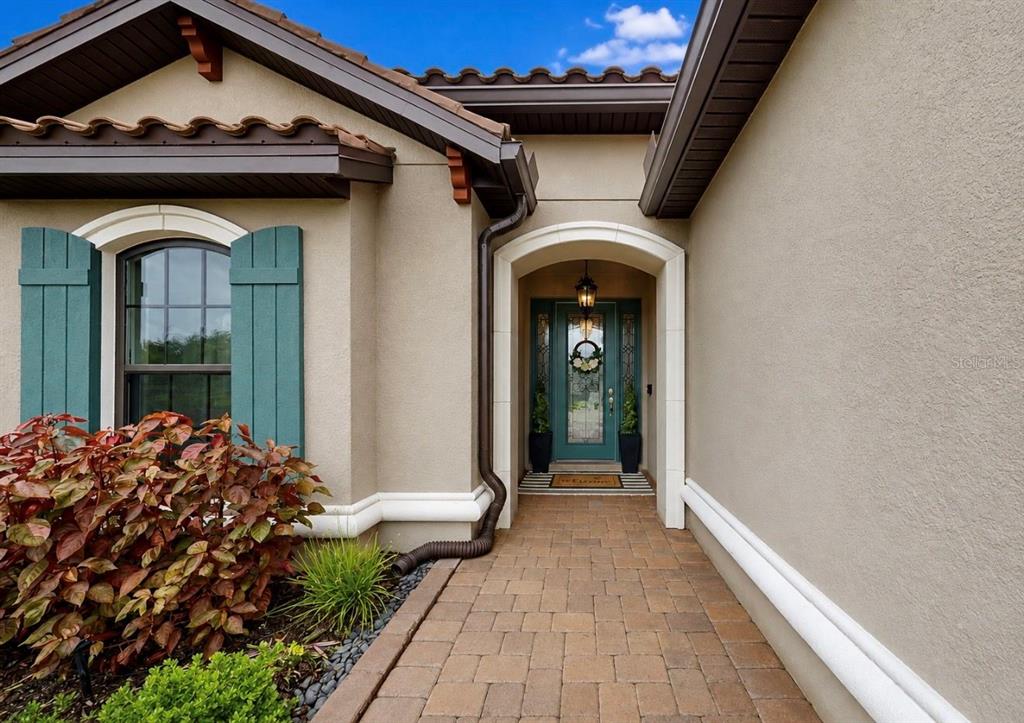 A paved walkway leads to the front entrance of a house with teal shutters — 10505 WICKER PARK PLACE, PALMETTO, FL