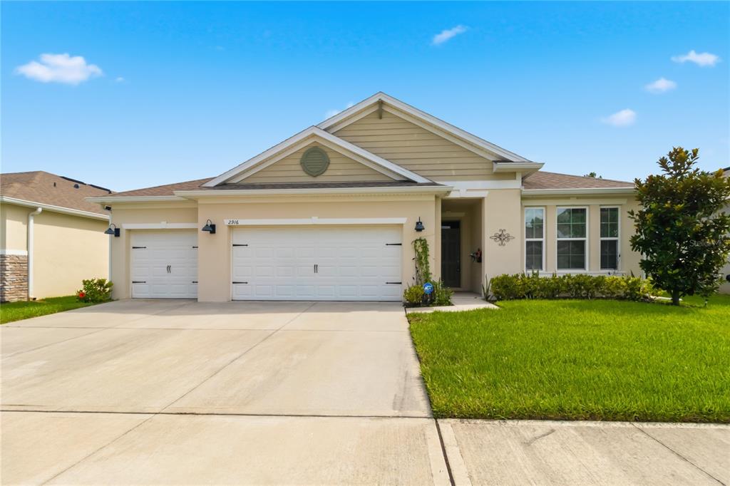 A single-story suburban house with a beige stucco exterior, a three-car garage, and a lawn — 2916 HOODED CRANE COVE, ST CLOUD, FL
