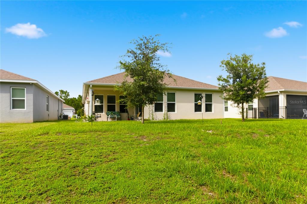 The rear exterior of a single-story house features a covered patio and a grassy yard — 2916 HOODED CRANE COVE, ST CLOUD, FL
